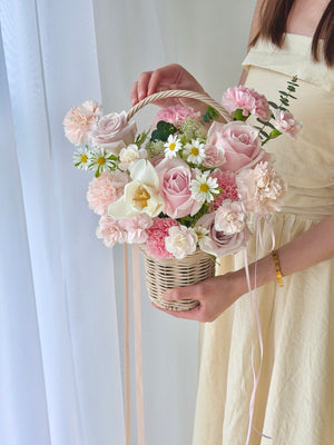 Person holding a basket of pink roses, white tulip, soft pink carnation and hana white against a white background perfect gift for Mother's Day.