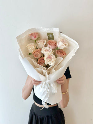 A woman stands by a window, holding a birthday bouquet of roses and cappuccino flowers in her Kuala Lumpur room.