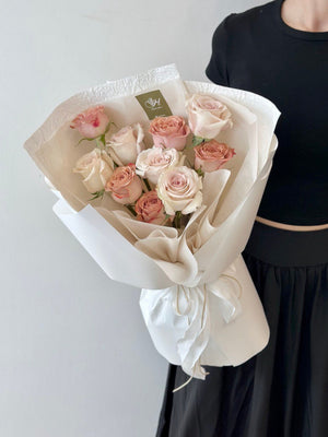 In her room in Kuala Lumpur, a woman presents a birthday bouquet of roses and cappuccino flowers in front of a window.