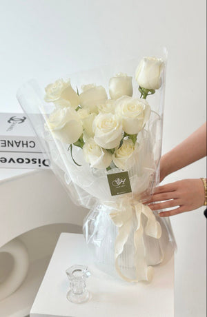 Eleven white roses arranged in a bouquet on a white column table next to a book in a Kuala Lumpur studio.