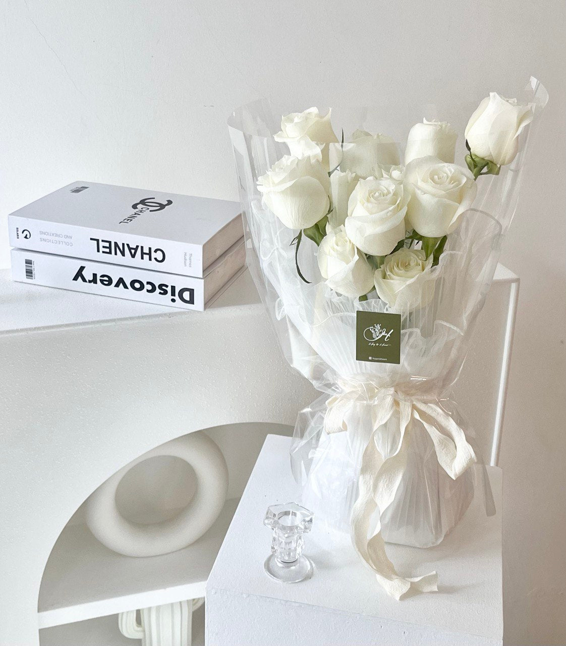 A bouquet of 11 white roses on a white column table beside a book in a studio room in Kuala Lumpur.