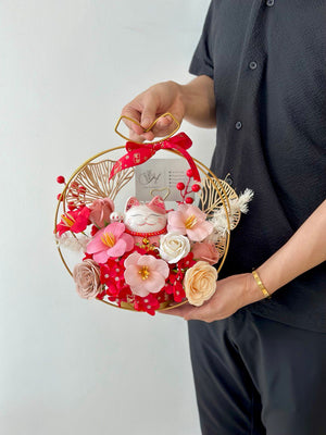 A table displays a gold ring filled with rose soap flowers and a card, alongside a pink lucky cat for a business opening event.