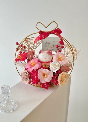 A gold ring filled with rose soap flowers and a card on a table, accompanied by a pink lucky cat for a business opening.