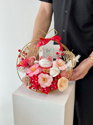 A gold ring filled with rose soap flowers and a card on it, with a pink lucky cat nearby for a business opening celebration.
