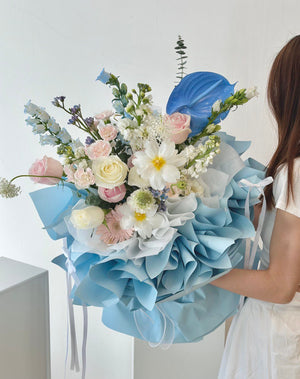 At her proposal event in Kuala Lumpur, a woman in a white dress holds a bouquet of blue and white flowers.