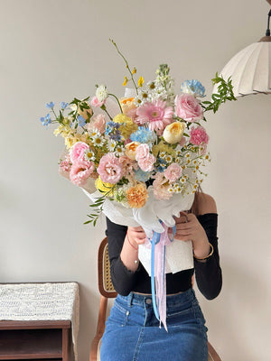 Person holding a bouquet of colorful flowers against a neutral background.