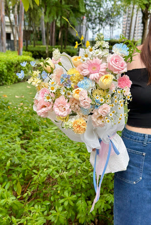 Person holding a large bouquet of flowers outdoors with greenery in the background.