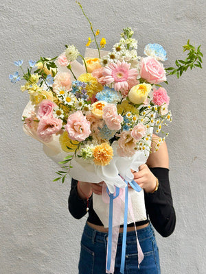 Person holding a bouquet of pastel flowers against a gray background perfect for birthday or anniversary flower.