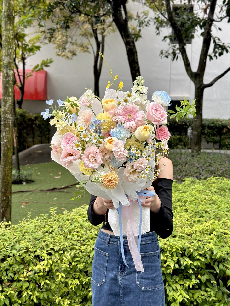 Person holding a bouquet of colorful flowers outdoors with greenery in the background.