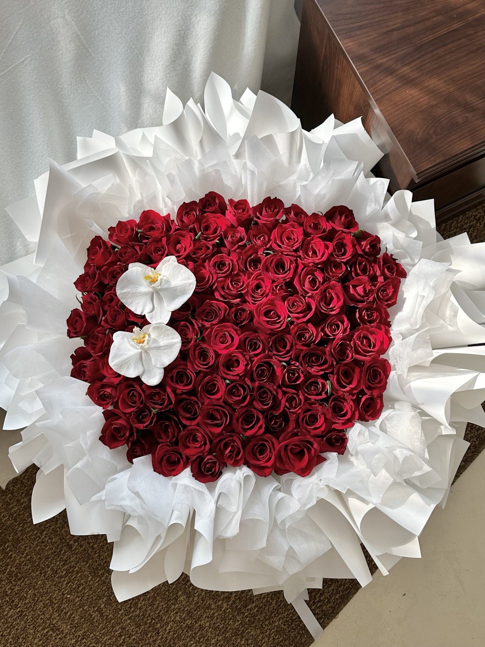 Heart-shaped arrangement of 99 red roses with white orchids on a white background