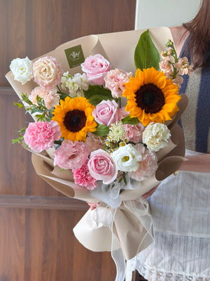 Bouquet of flowers with sunflowers held by a person, against a wooden background at Sunway Geo.