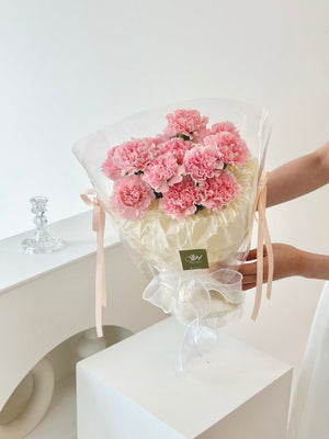 A woman lovingly holds a bouquet of pink carnations, intended as a Mother's Day gift for her mother in 2025.