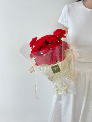 A girl wearing a white top holds a red carnation bouquet, honoring her mother on Mother's Day 2025.