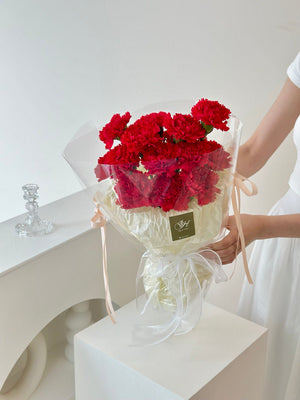 A young woman in a white top presents a red carnation bouquet for Mother's Day 2025.