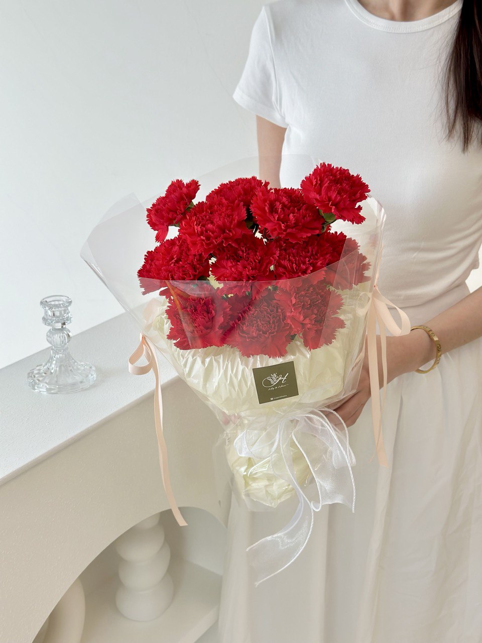 A girl wearing white t-shirt is holding a beautiful red carnation bouquet for her mother during mother's day 2025