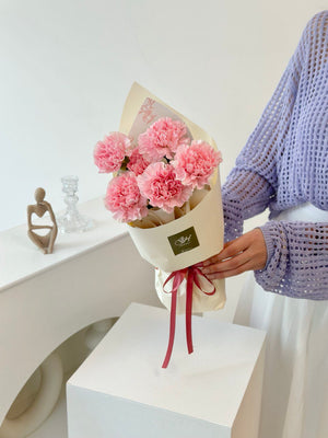 A young girl wearing a purple cardigan presents a bouquet of pink carnations for Mother's Day 2025.