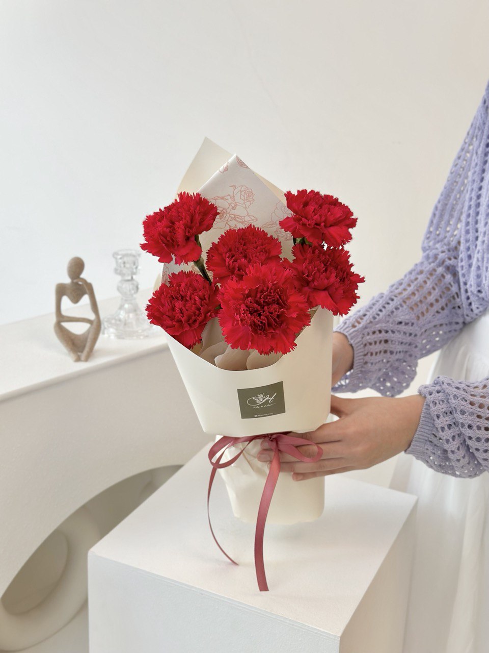 A young woman in a purple cardigan presents 1 bouquet of red carnations for Mother's Day 2025.