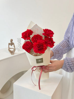 A young woman in a purple cardigan presents 1 bouquet of red carnations for Mother's Day 2025.