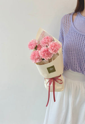 A girl in a purple cardigan joyfully holds pink carnations, honoring her mother on Mother's Day 2025.