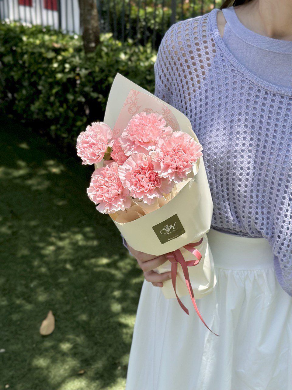 A girl in a purple cardigan holds a bouquet of pink carnations, celebrating Mother's Day 2025 with love.