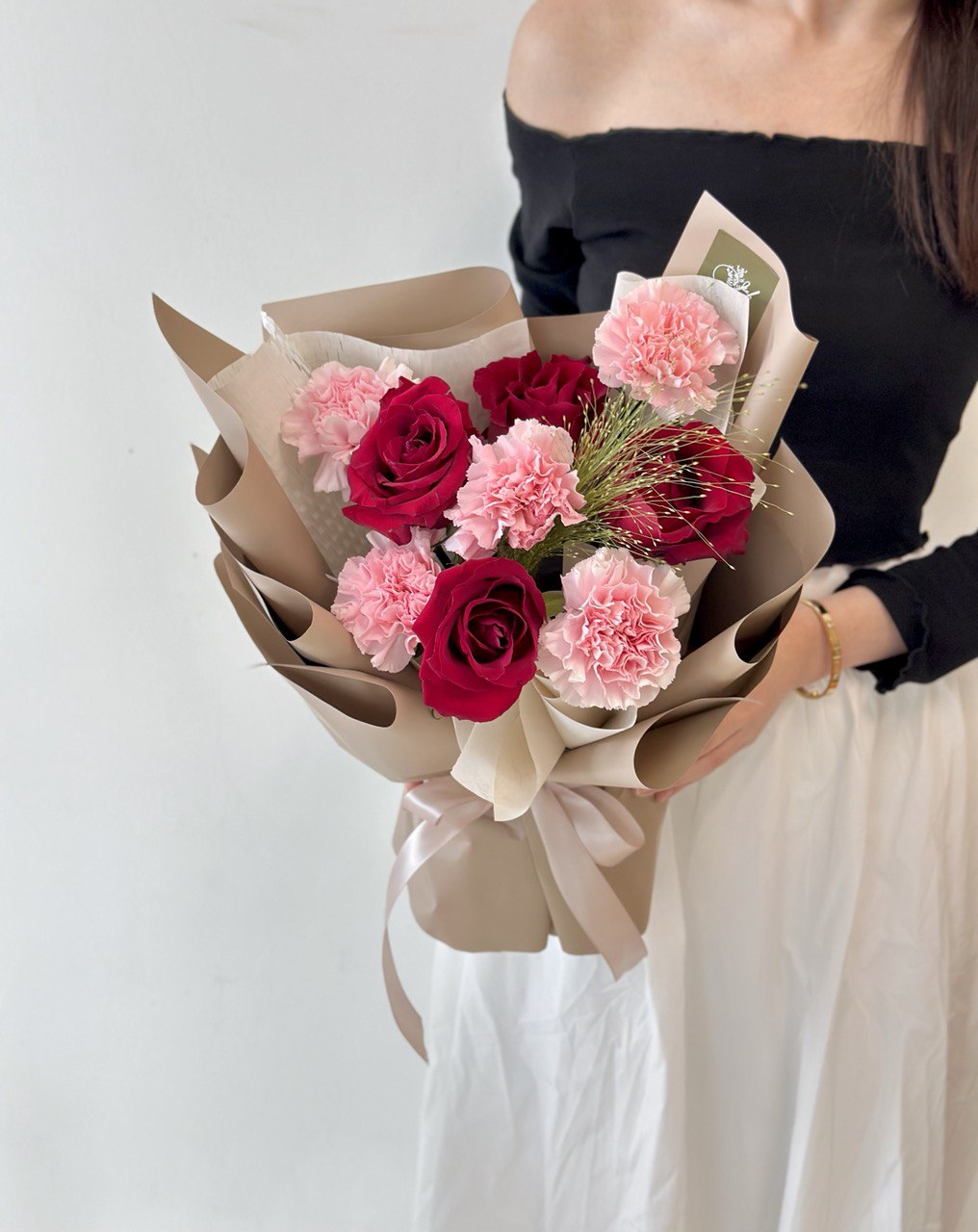 In Kuala Lumpur, a woman dressed in a black top and white jeans holds a Mother's Day bouquet of red rose and pink carnations.