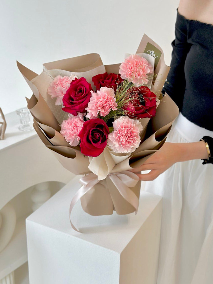 A woman in a black top and white jeans holds a Mother's Day bouquet of red rose and pink carnations in Kuala Lumpur.