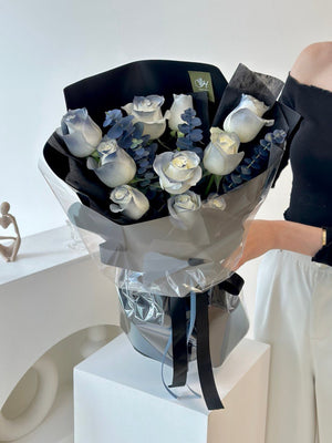A woman in a room in Kuala Lumpur holds a bouquet of white roses, showcasing her joyful expression.