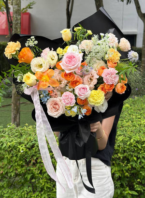 Vibrant orange and pink rose bouquet wrapped in black paper, perfect for celebrations and gifts.