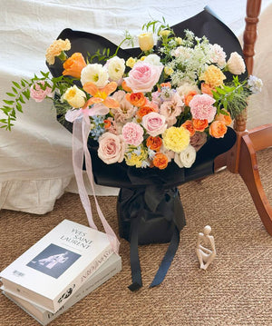 Elegant mixed flower bouquet featuring roses, carnations, and tulip in warm pastel tones with black wrapper.