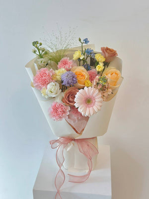 A colorful bouquet of flowers is placing on top of a white box for a photoshoot for Mother's Day 2025.