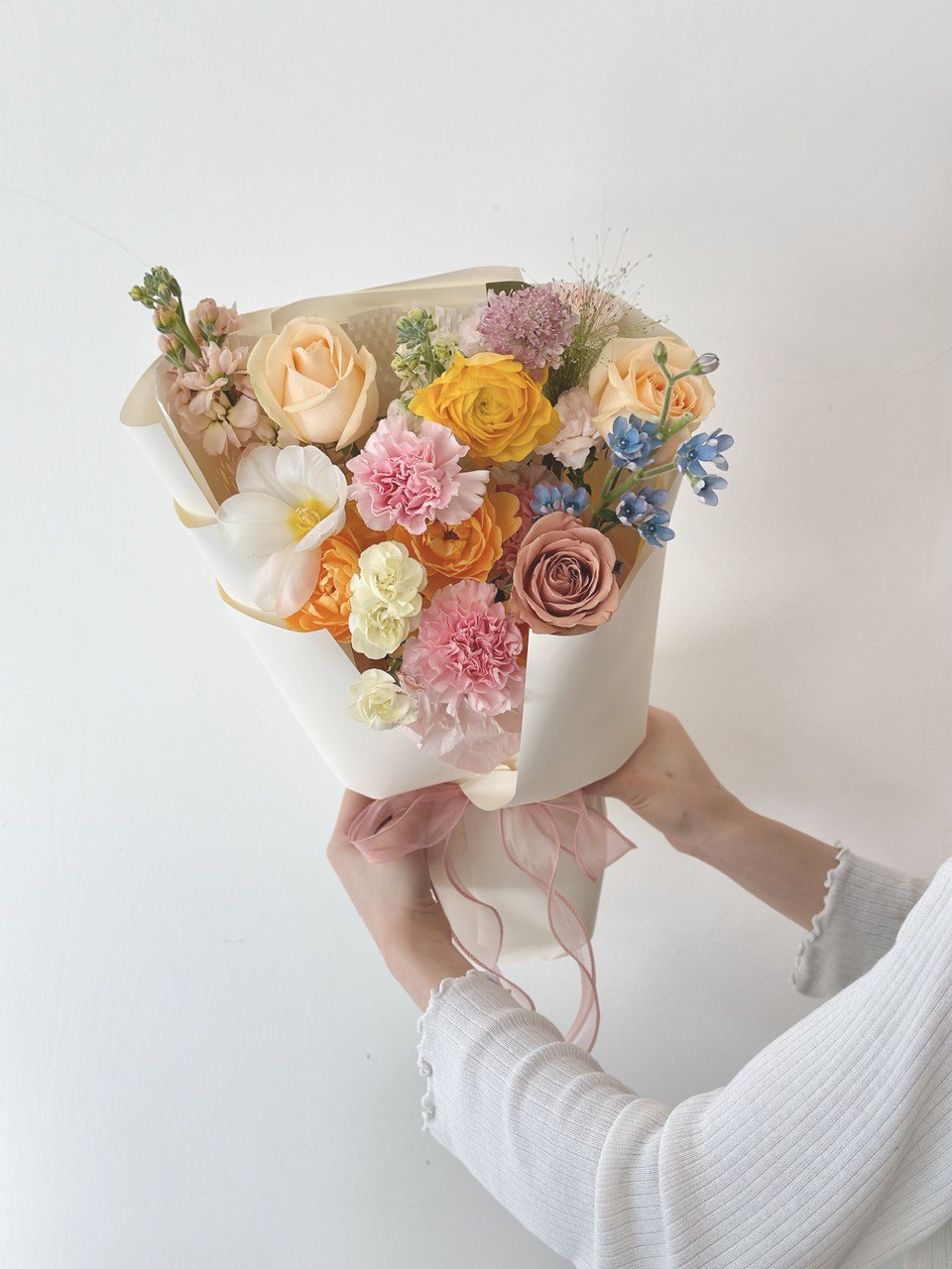 A girl with white cardigan is holding a colourful flower bouquet for her mother during Mother's Day 2025.