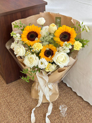 Bouquet of sunflowers and white roses in brown paper packaging on a carpeted floor.