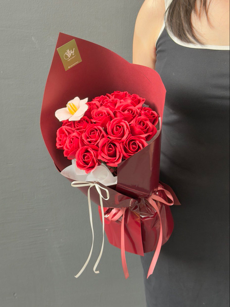 Bouquet of red roses soap flower with a peach soap tulip flower in a red wrap held by a person against a gray background with same day delivery at Kuala Lumpur prepared by hug and heart florist.