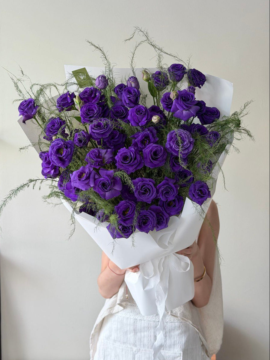 Bouquet of purple eustoma flowers held by a person against a white background at Hug and Heart Florist Subang Jaya Selangor.