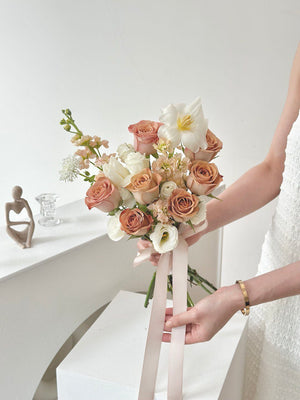 A woman in a white wedding dress holds a bouquet of Cappuccino Roses and holding a ribbon in a studio.
