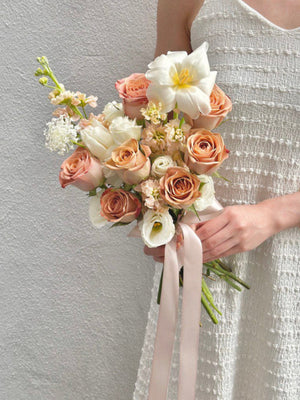 A woman in a white wedding dress holds a bouquet of Cappuccino Roses, set against the backdrop of Kuala Lumpur.