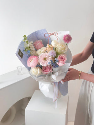 A woman in a black top holds a pink bouquet with blue wrapping, celebrating her birthday in her studio.