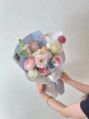 A girl in a black top presents a pink pastel bouquet with blue wrapping, celebrating her birthday in her studio.