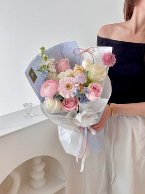 A woman wearing a black top holds a pink pastel bouquet wrapped in blue, celebrating her birthday in her studio.