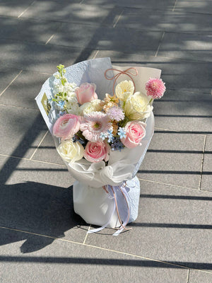 A pink pastel bouquet wrapped in blue is place on a floor with a glaze of sunlight.