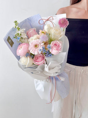A woman in a black top holds a pink pastel bouquet with blue wrapping in her studio for her birthday celebration.