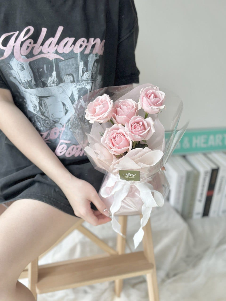 A person holding a bouquet of pink roses wrapped in clear plastic with a white ribbon - same day flower delivery at Kuala Lumpur.