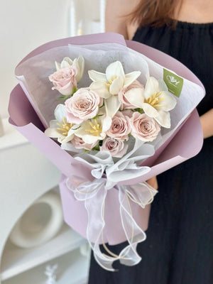 A bouquet of flowers including menta roses and white tulips, wrapped in a pale purple wrapper with a decorative ribbon.