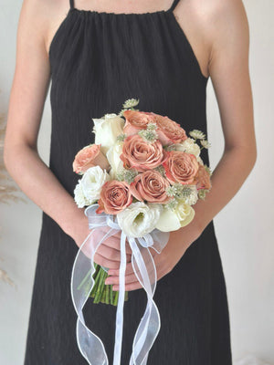 A person holding a bouquet of flowers which includes shades of pink and white roses, with green leaves and decorative ribbon for bridal.