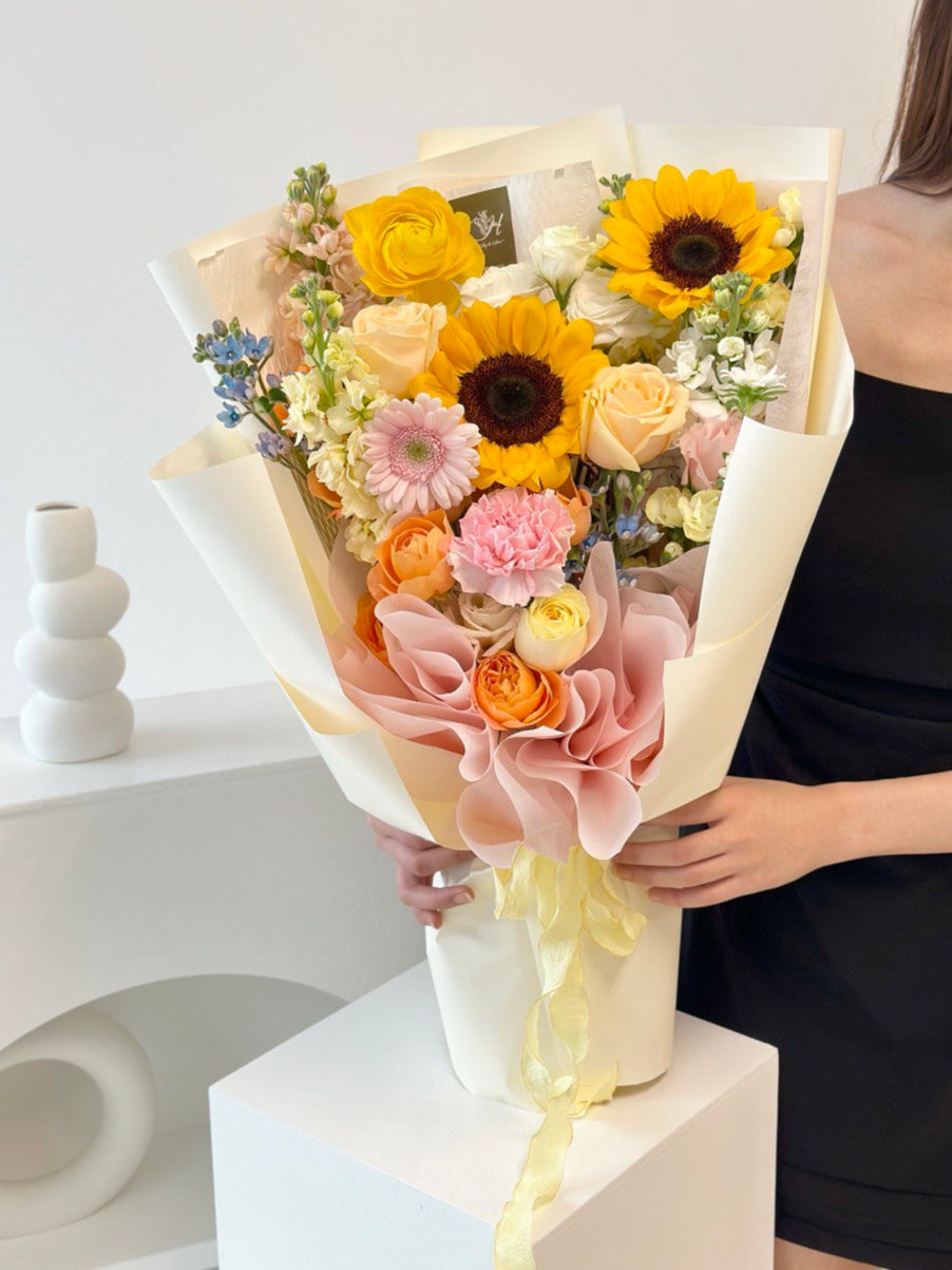 A woman in a black gown joyfully holds a bouquet of sunflowers at her graduation ceremony.
