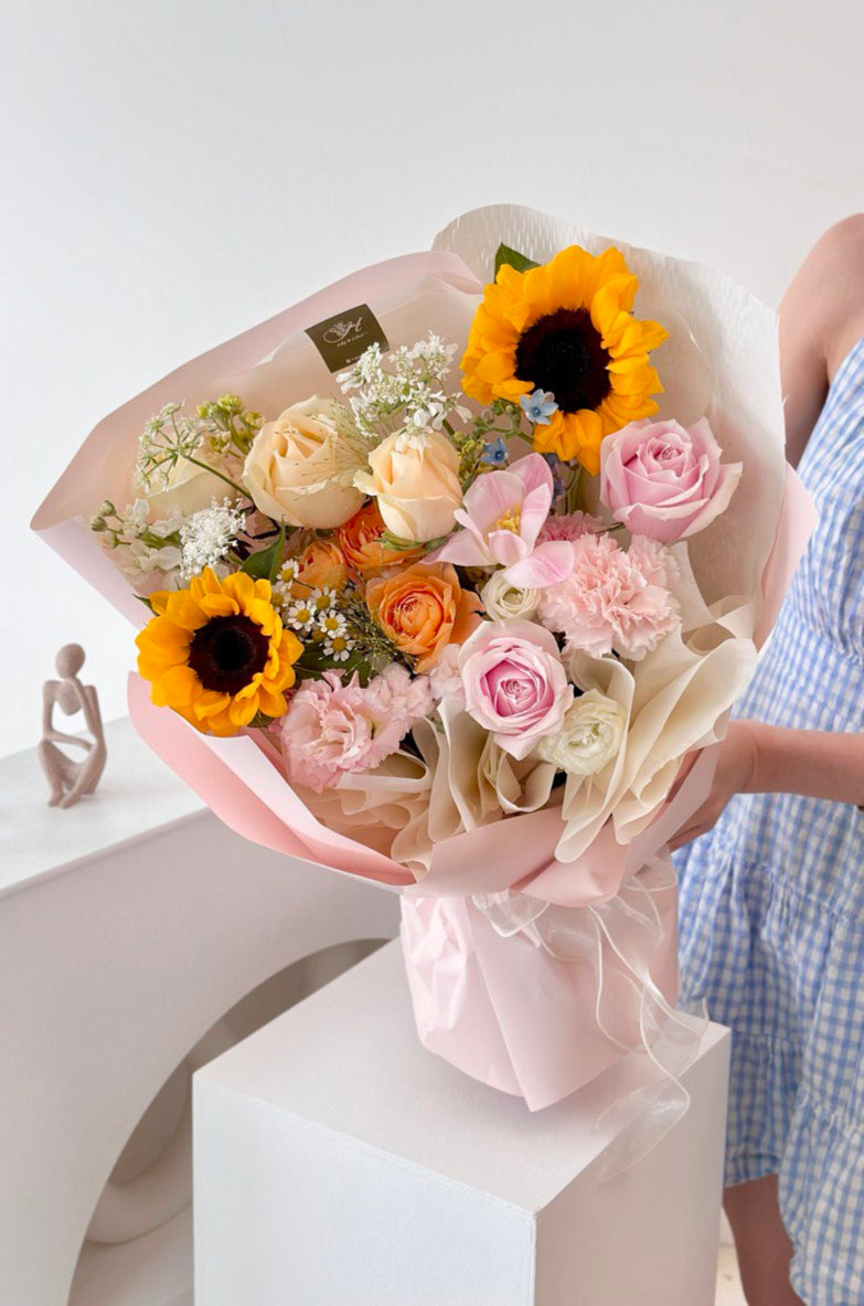 A woman in a blue dress celebrates her graduation in Kuala Lumpur, holding a bouquet of sunflowers.
