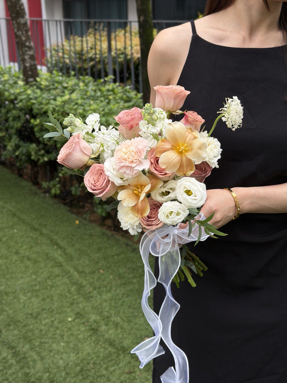 Bouquet of cappuccino ROM flowers held by a person wearing a black sleeveless top, with a blurred outdoor background.