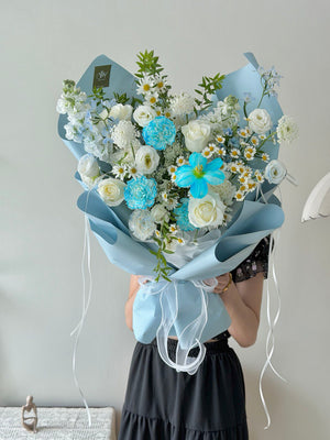 Bouquet of  flower consist of blue tulip, blue carnation, white roses and white fillers held by a person against a plain background.