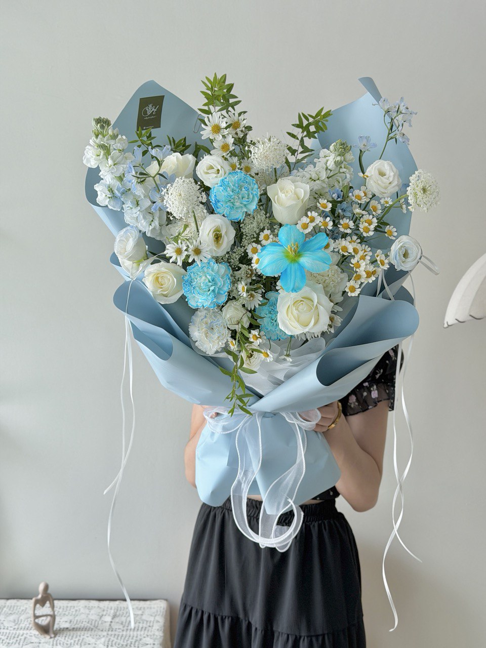 Bouquet of  flower consist of blue tulip, blue carnation, white roses and white fillers held by a person against a plain background.