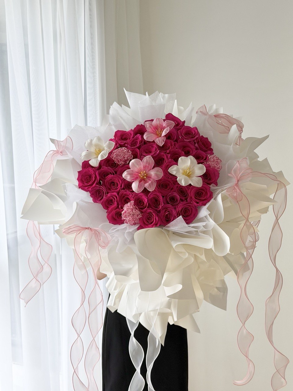 A girl is holding a heart-shaped bouquet of hot pink roses with with tulips and carnation wrapped in white ballet wrapper with pink ribbons.
